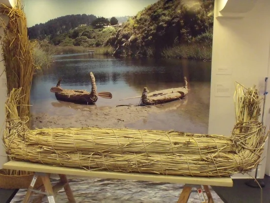 A working example of an Ohlone Tule Boat, pictured with another in the water as a background